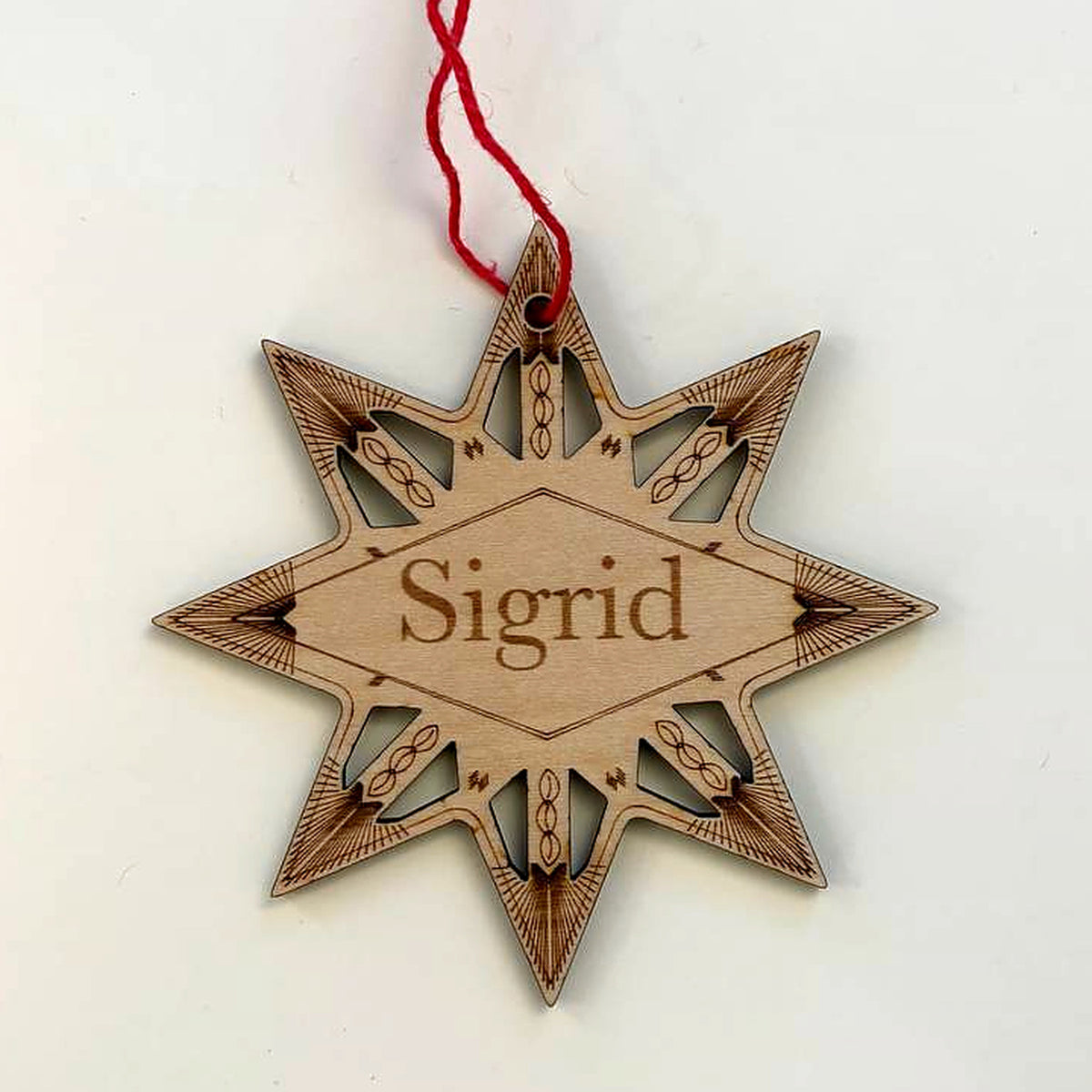 Winter star Christmas ornament in laser-cut birch wood, engraved with the sample name Sigrid, hanging from a red cord