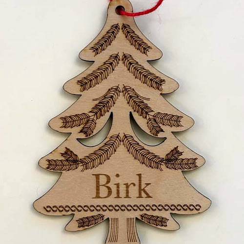 Close view of the evergreen tree ornament: the engraved name Birk, engraved branches and the natural birch wood grain