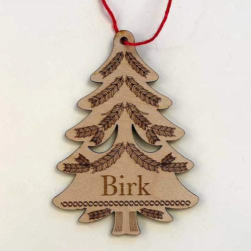 Evergreen tree Christmas ornament in laser-cut birch wood, engraved with the sample name Birk, hanging from a red cord