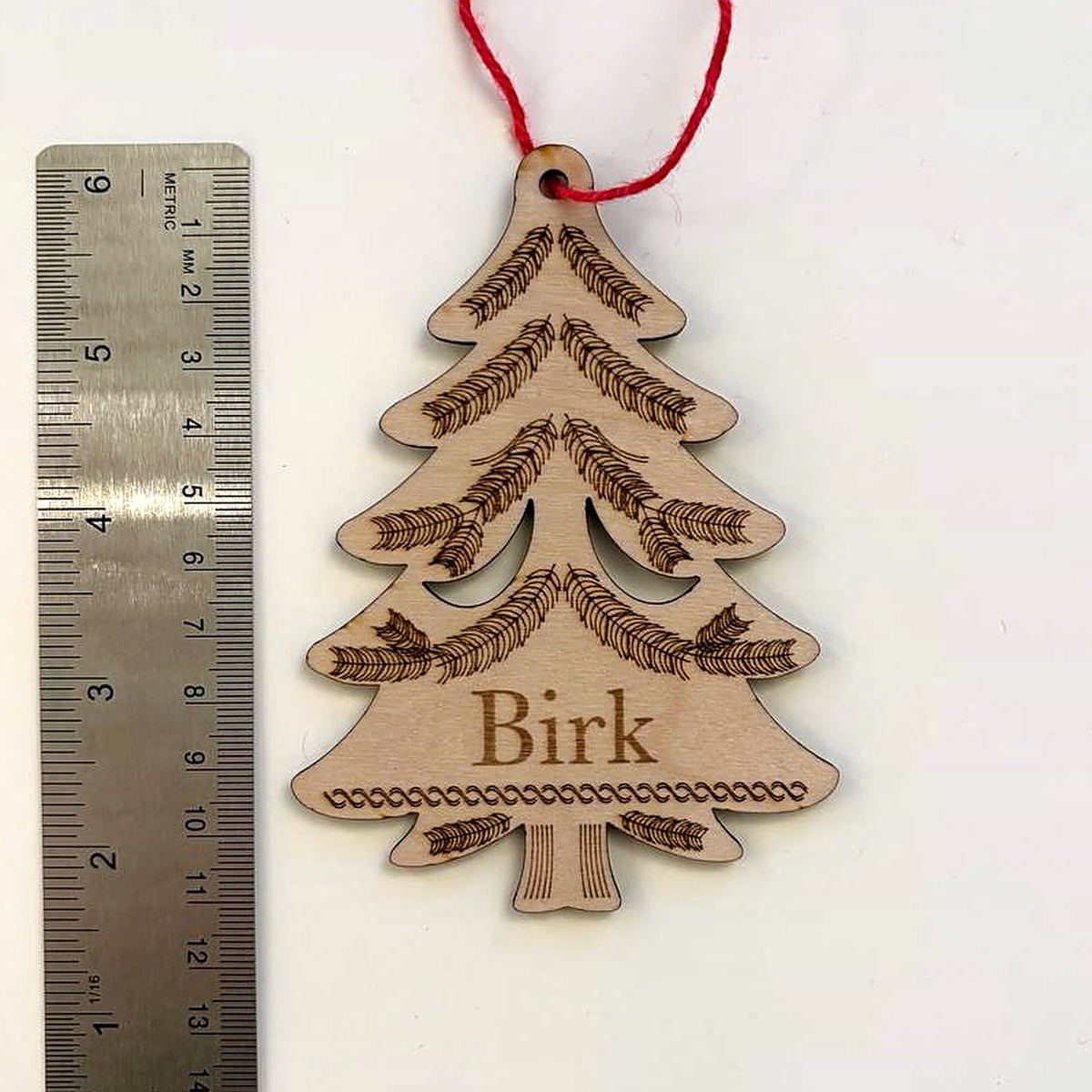 Evergreen tree name ornament photographed beside a metal ruler to show its size