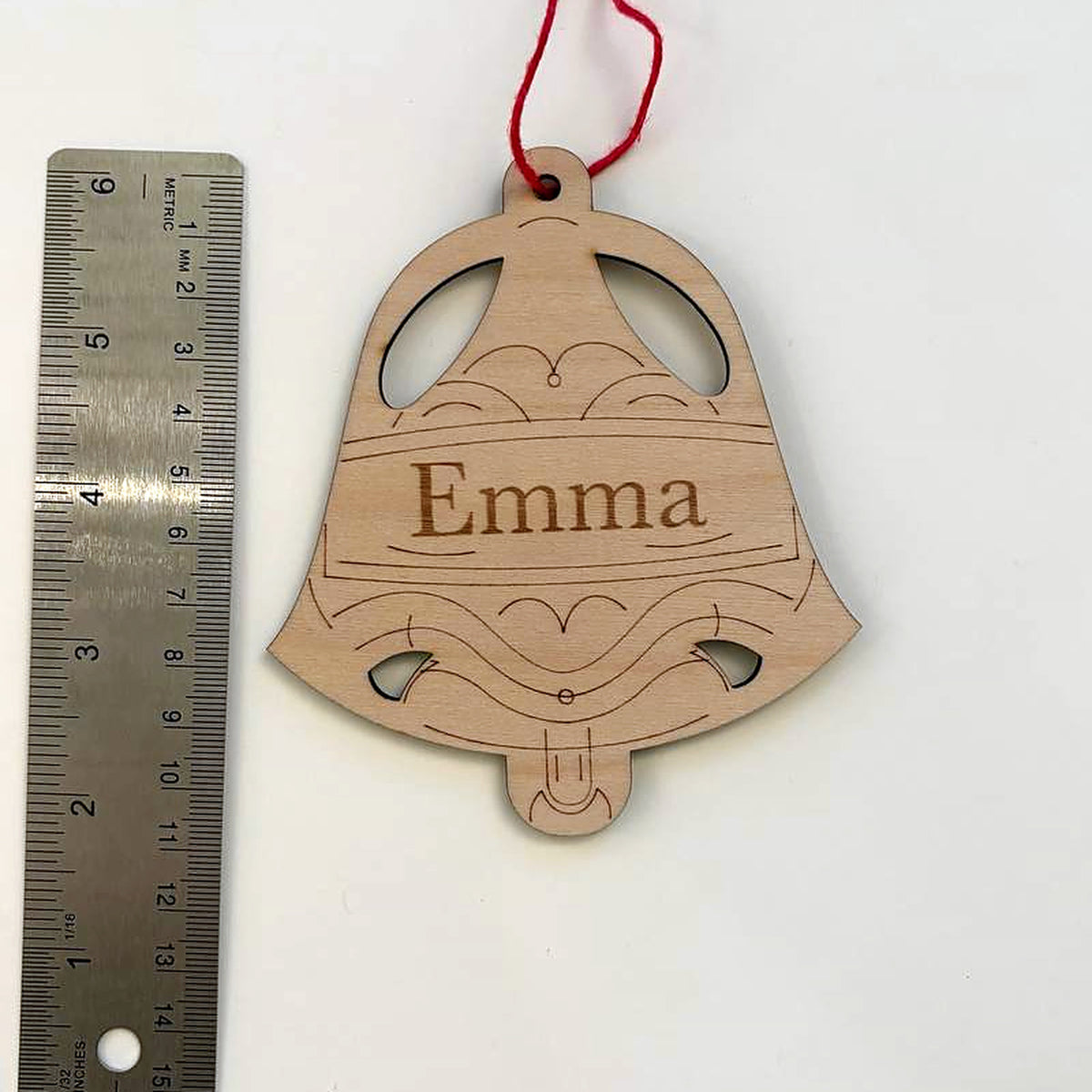 Winter bell name ornament photographed beside a metal ruler to show its size