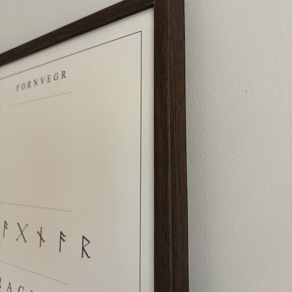 Close detail of the wood frame edge, paper, and printed rune inscription.